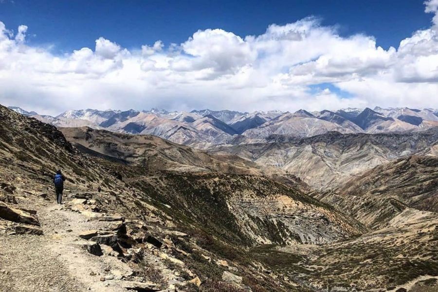 Solo trekker on rocky trail with expansive Himalayan mountain views